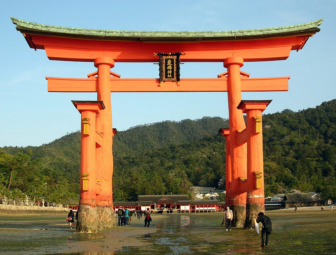 The Great Torii Gate of Itsukushima Shrine at low tide, with visitors walking on the exposed seabed towards it.