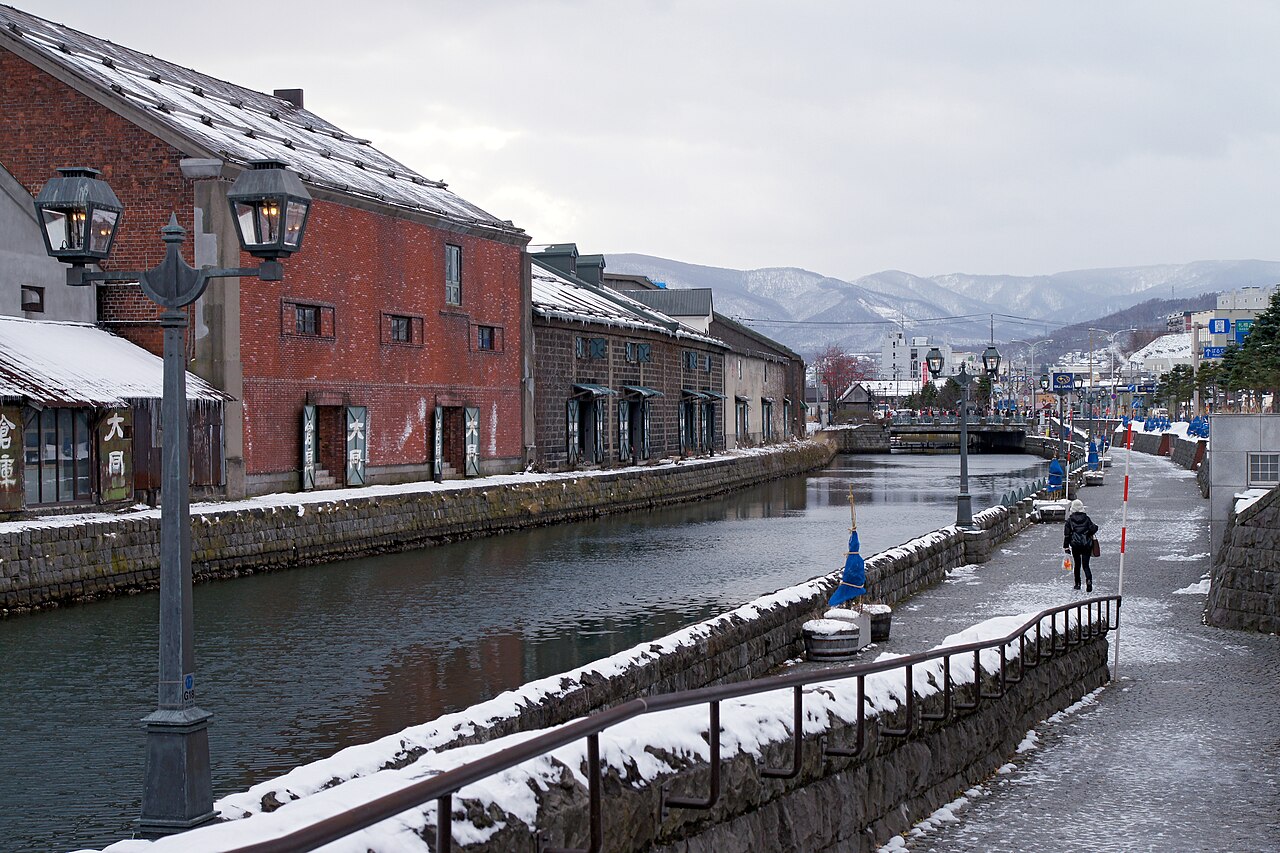 Historic Otaru Canal lined with stone warehouses and illuminated gas lamps, reflecting in the water.