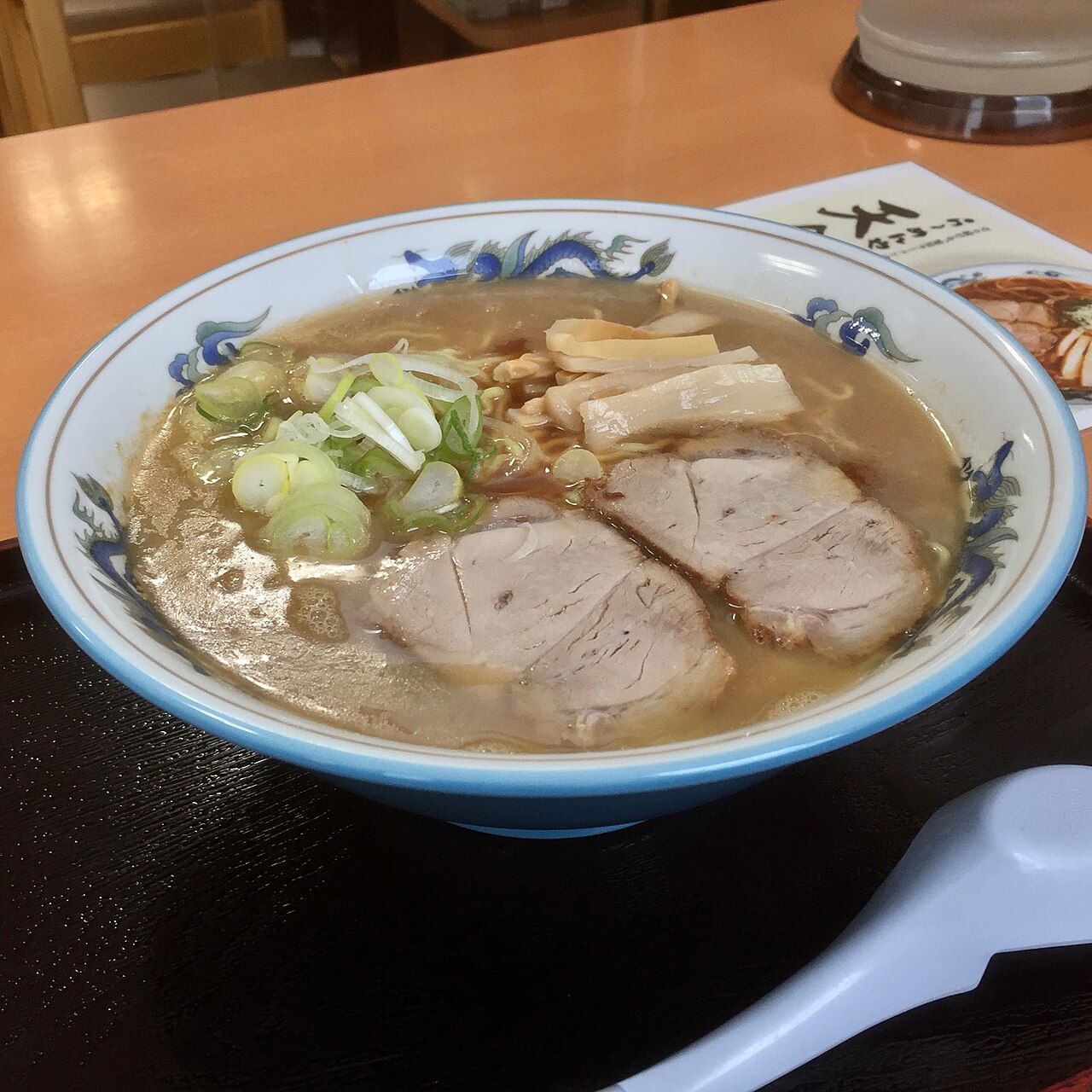 A bowl of Asahikawa shoyu ramen with a clear, soy-based broth, chashu, and green onions.