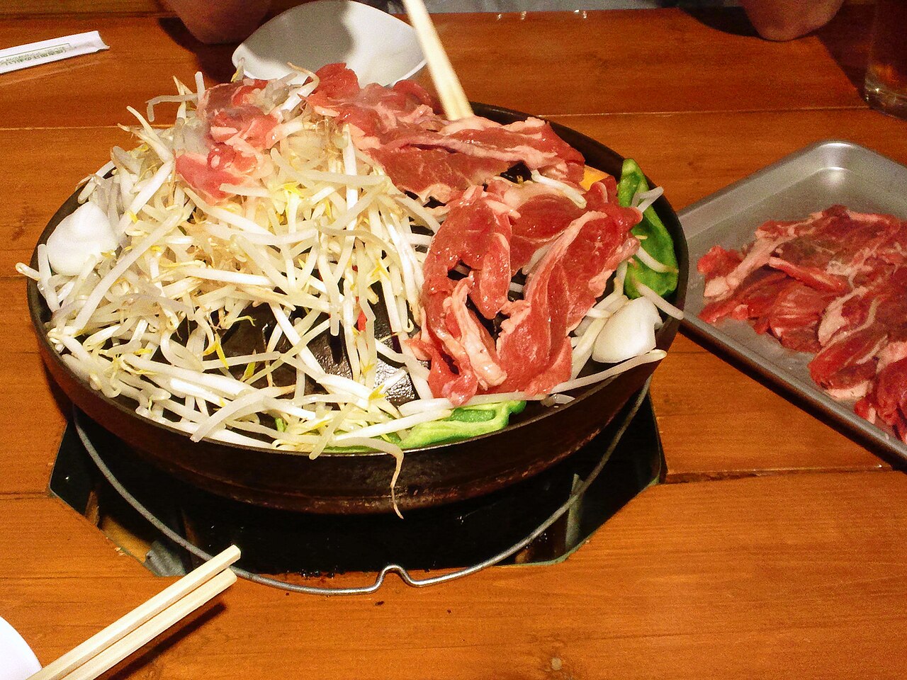 Slices of lamb grilling on a dome-shaped jingisukan grill, surrounded by vegetables.