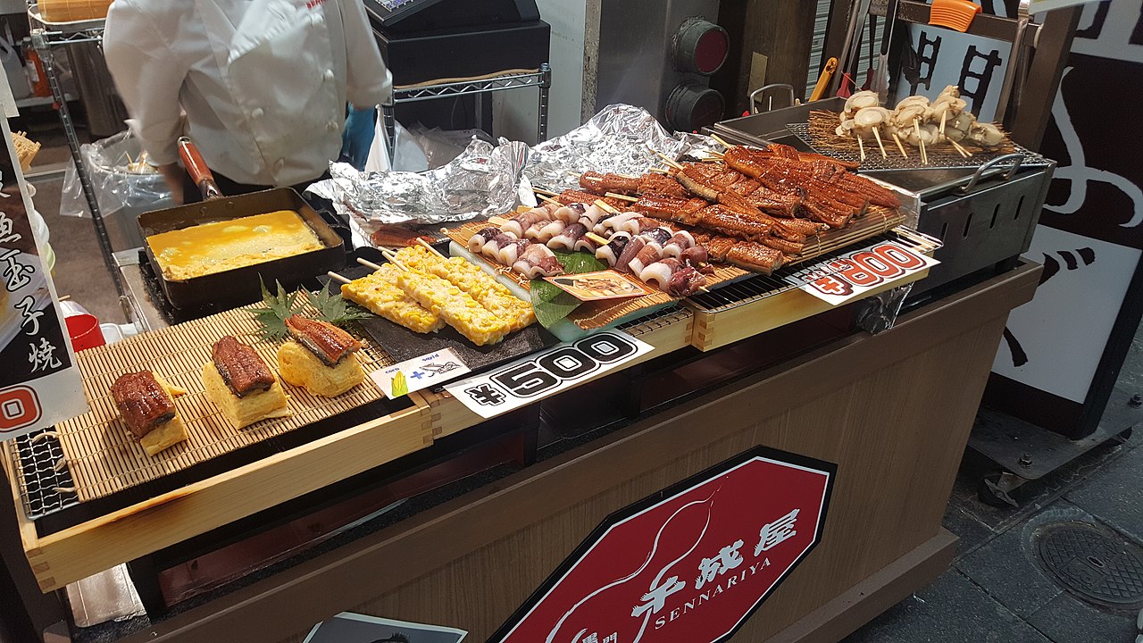 A bustling scene of various food stalls and fresh produce at Kuromon Market, showcasing the wide selection of dishes available.