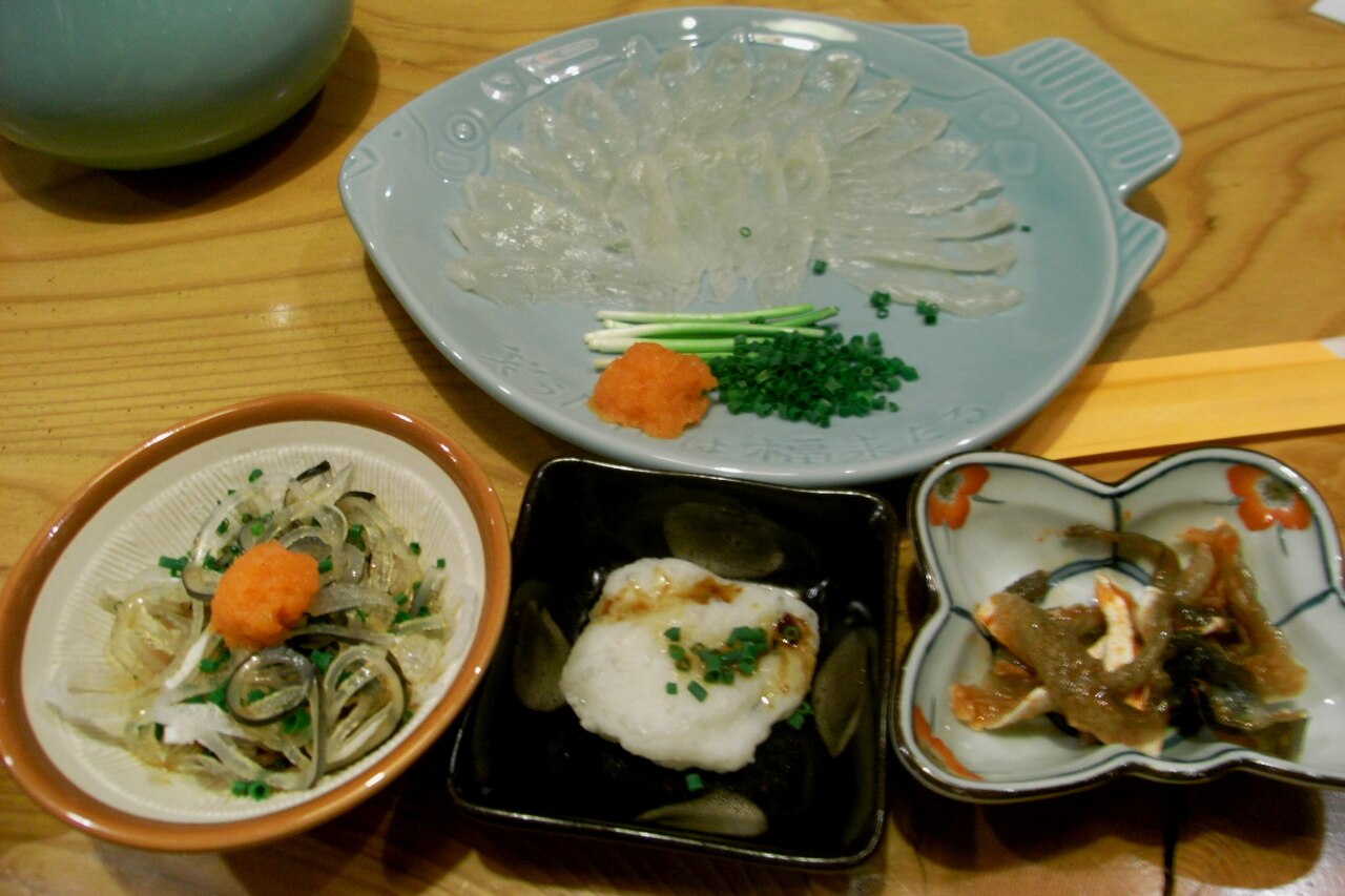 Delicately sliced fugu (pufferfish) sashimi arranged on a plate, a seasonal specialty at Kuromon Market.