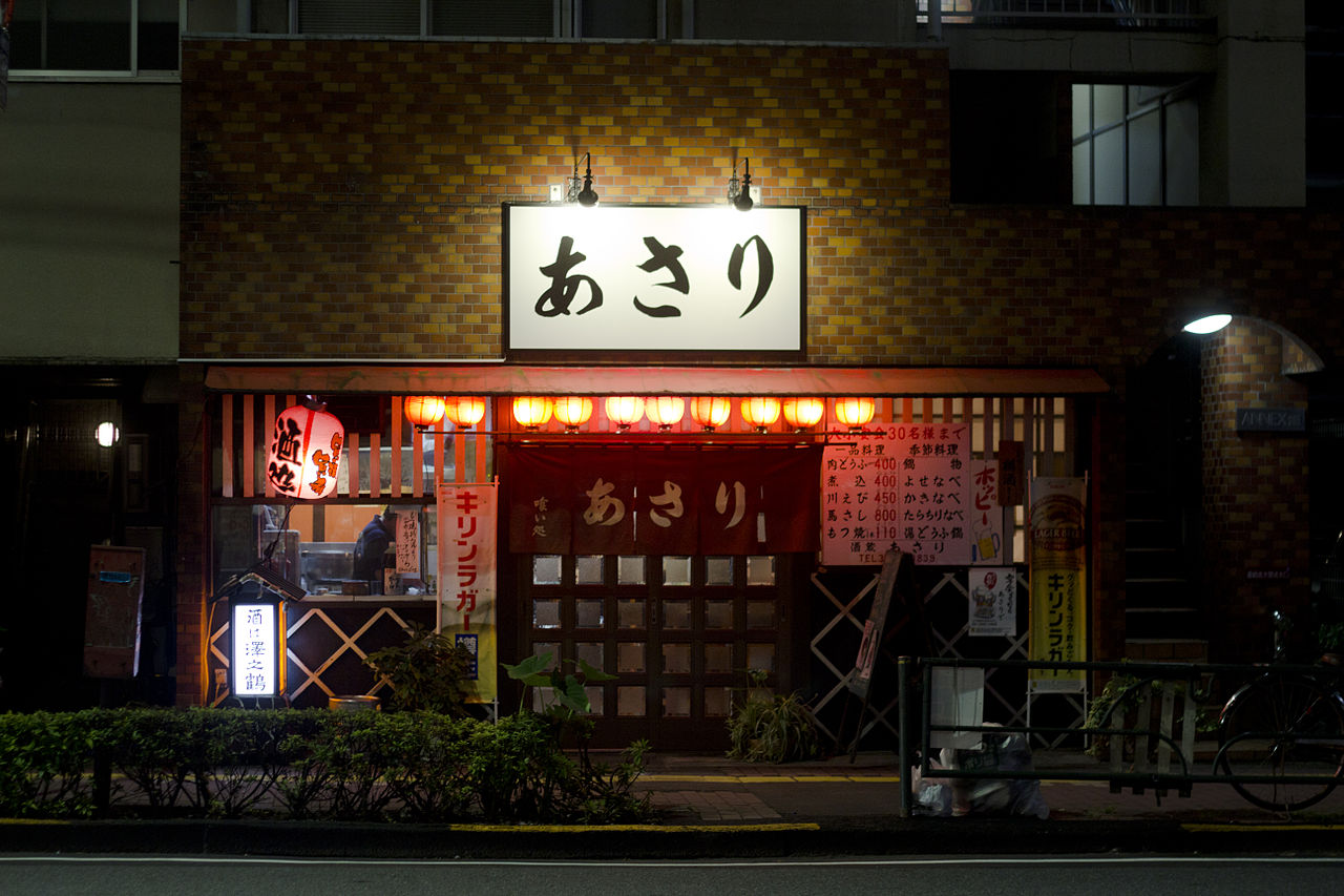 Assortment of small plates and drinks on a table inside a lively Japanese izakaya