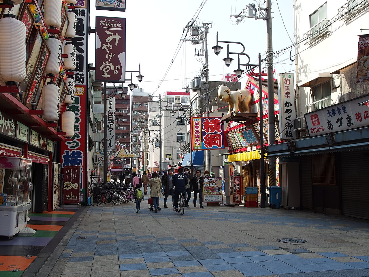 Vibrant Shinsekai street with Tsutenkaku Tower in the background, bustling with food stalls