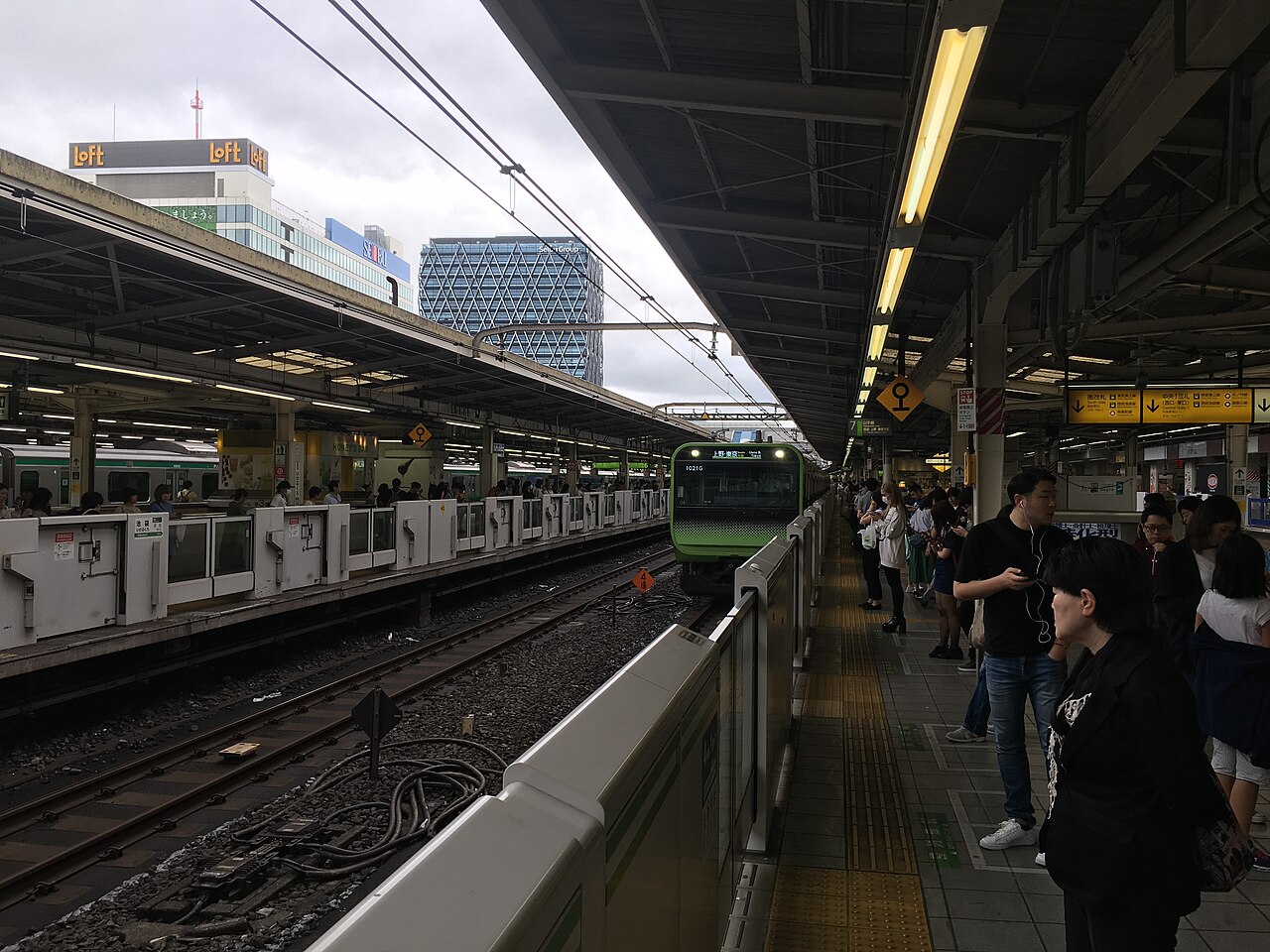A green JR Yamanote Line train arriving at a Tokyo station platform.