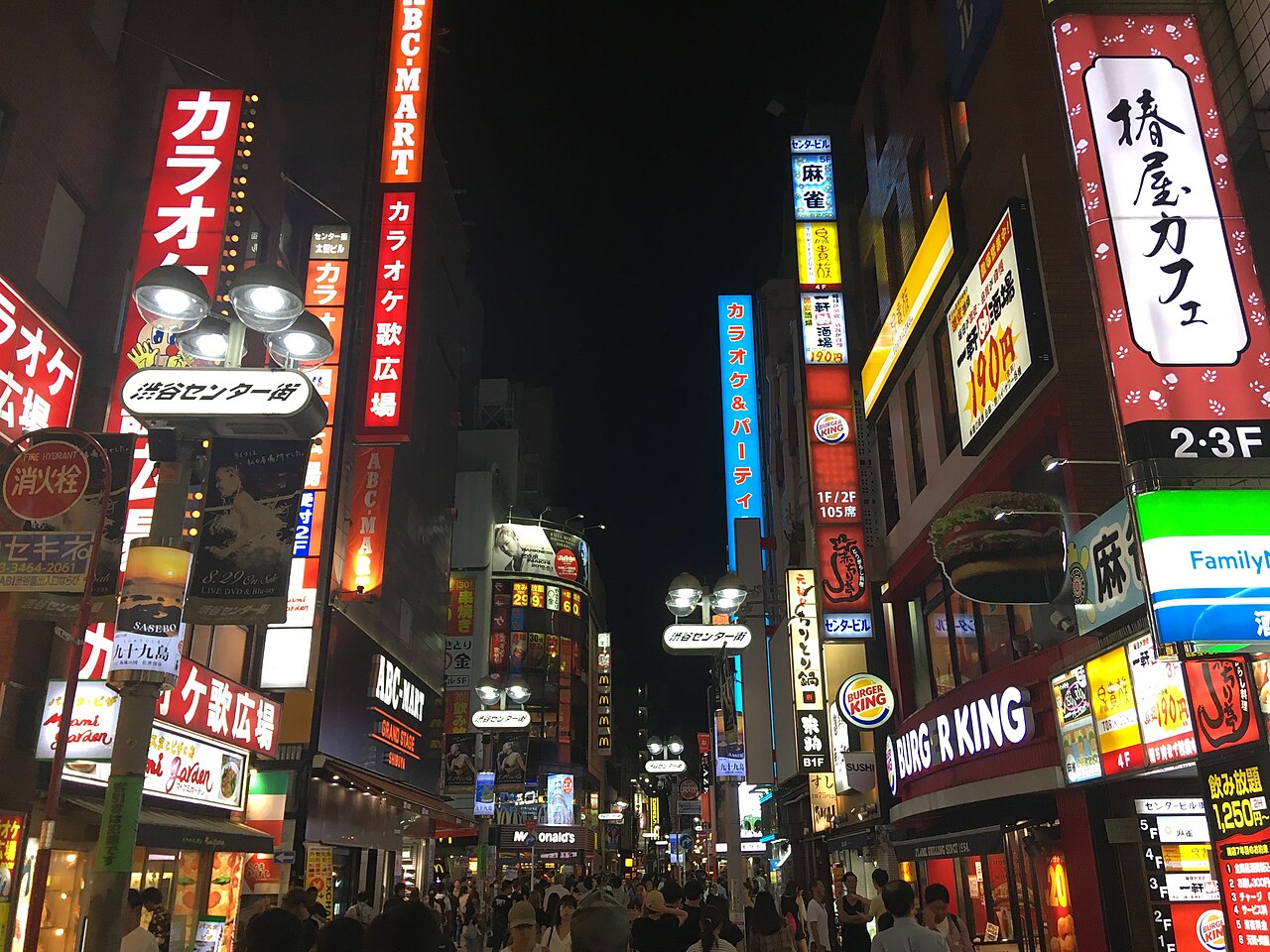Busy street scene in Shibuya Center-gai at night, with shops and neon signs