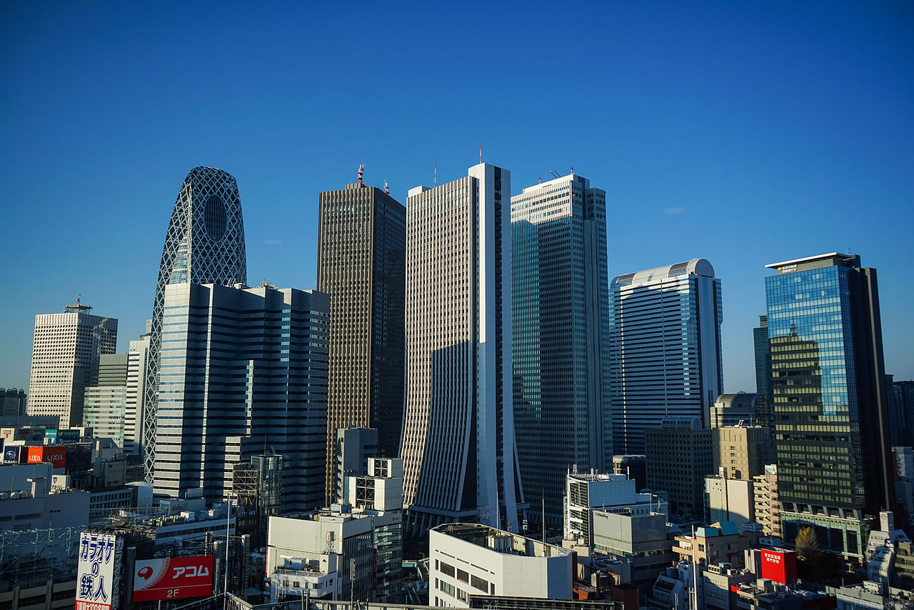 Panoramic view of Shinjuku skyline from Tokyo Metropolitan Government Building observation deck, showing skyscrapers and distant mountains.