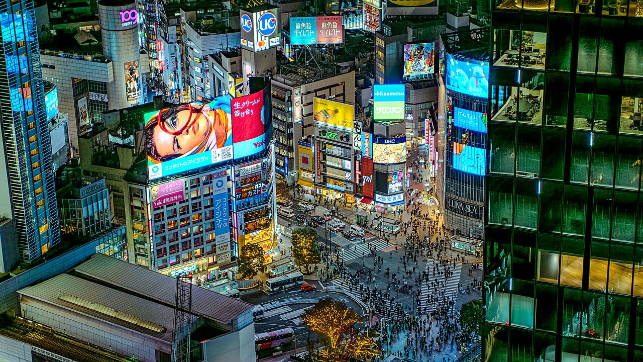 Aerial view of Shibuya Crossing at night, bustling with pedestrians and neon lights