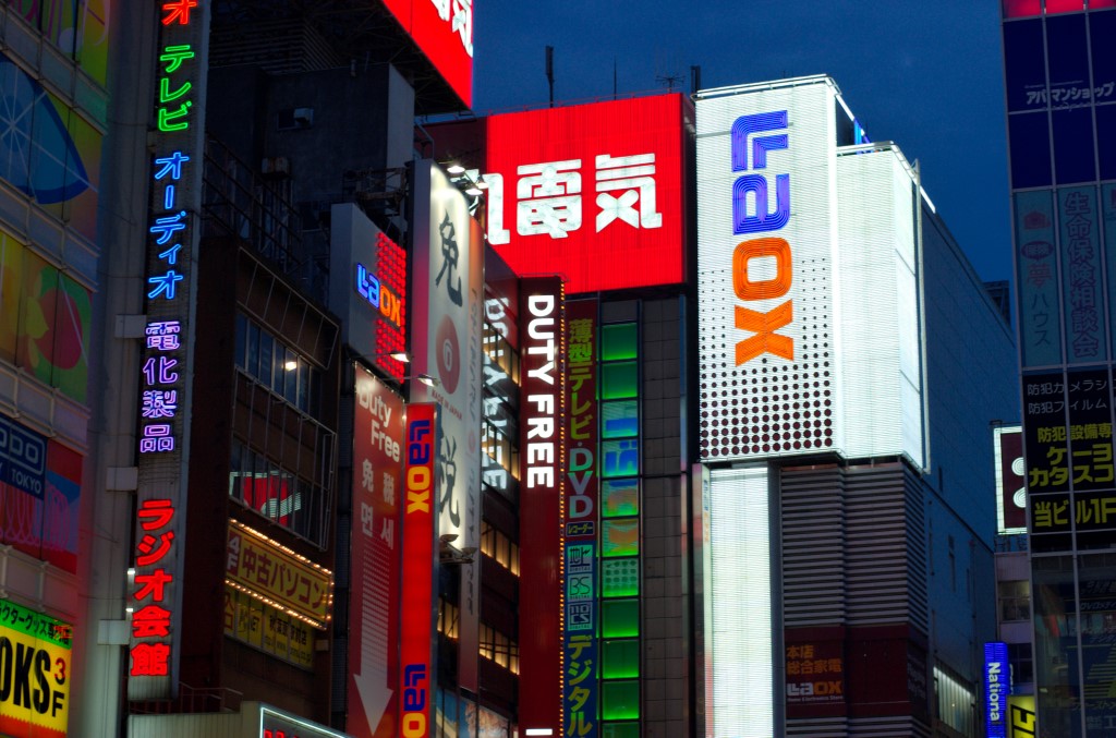 Vibrant street scene in Akihabara Electric Town at night, with towering buildings illuminated by colorful neon signs