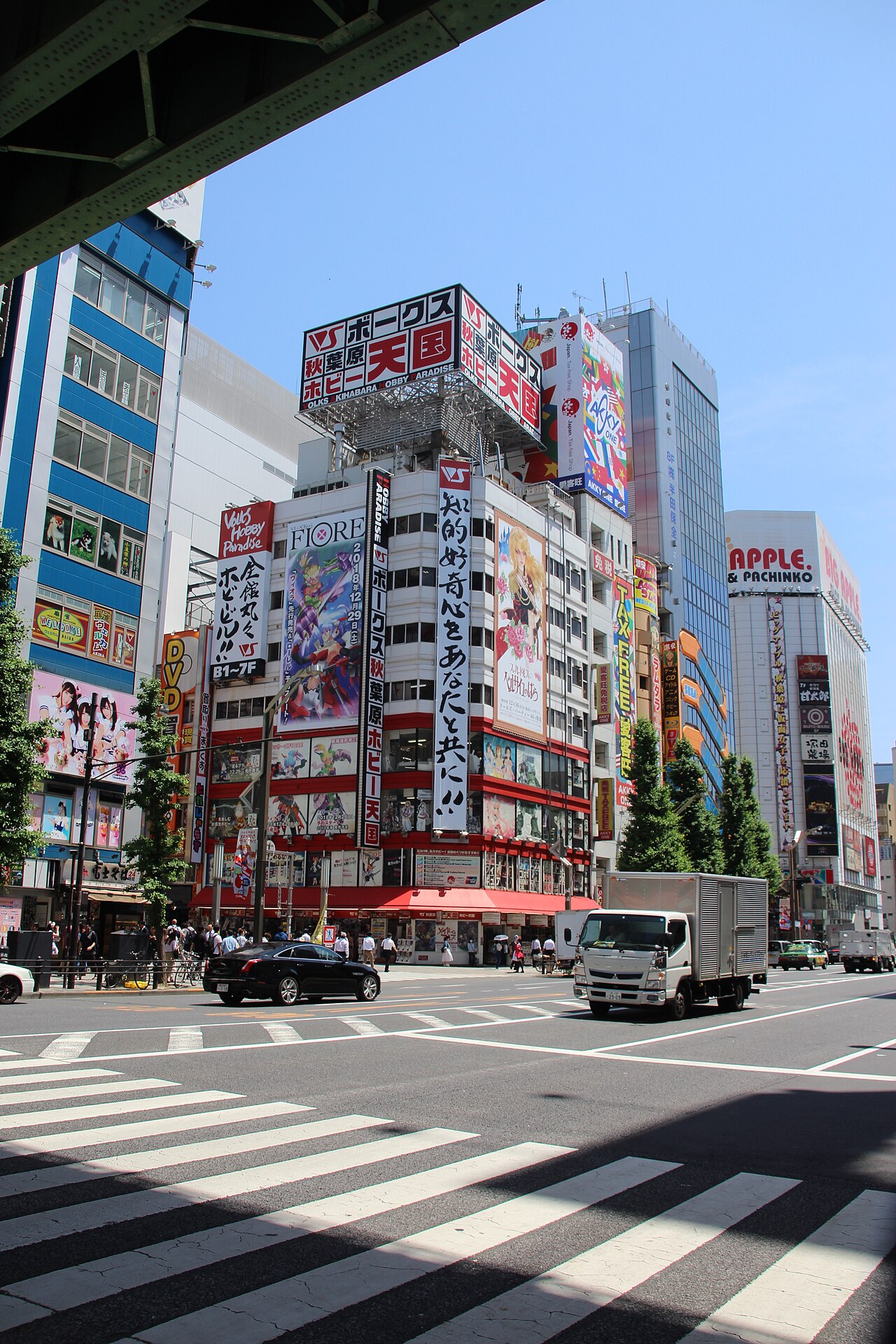 A vibrant night view of Akihabara's main street, illuminated by countless neon signs and electronic store displays.
