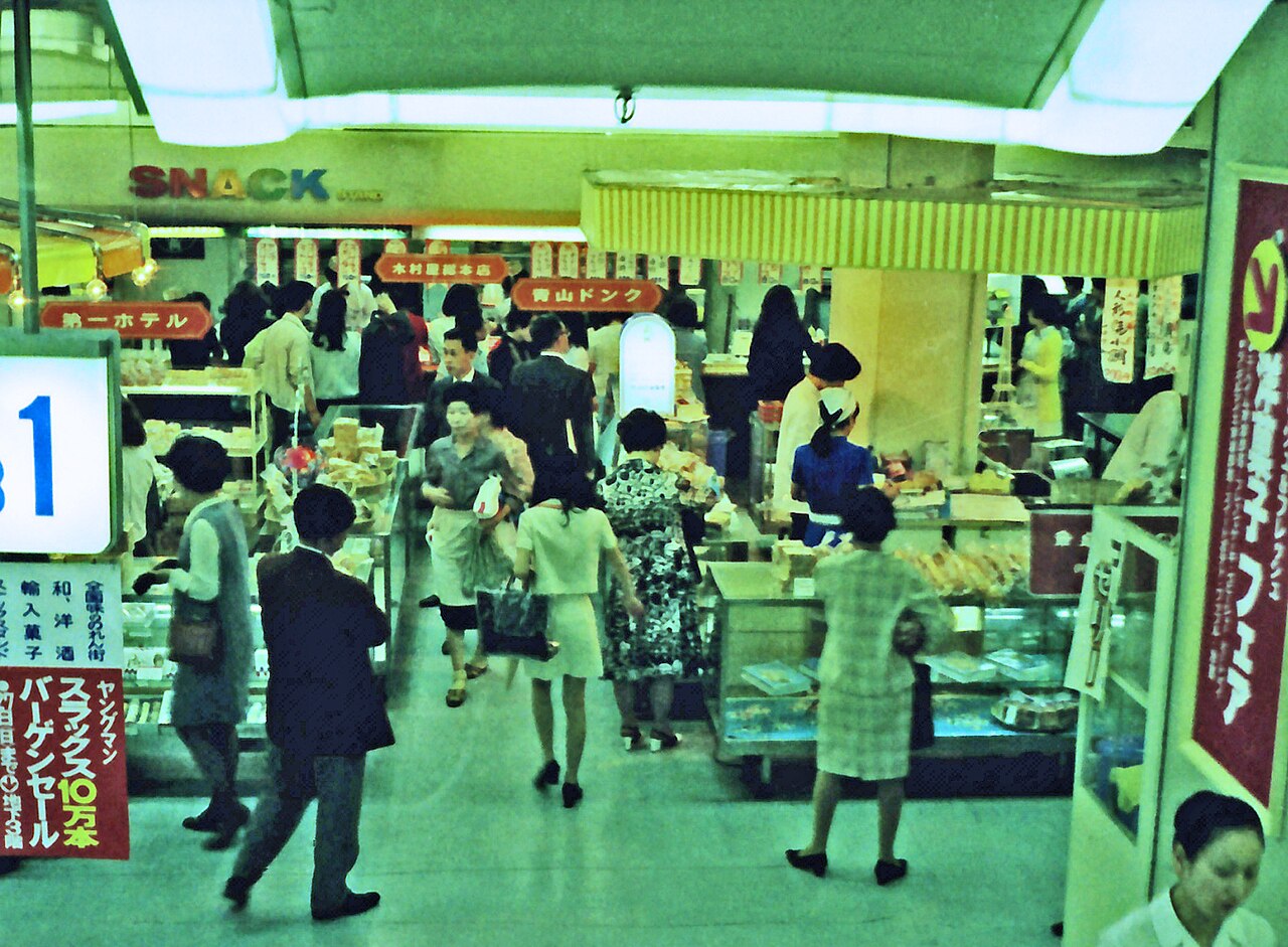 A spacious, modern indoor shopping complex in Tokyo with multiple floors and natural light, bustling with people, offering a dry refuge on a rainy day