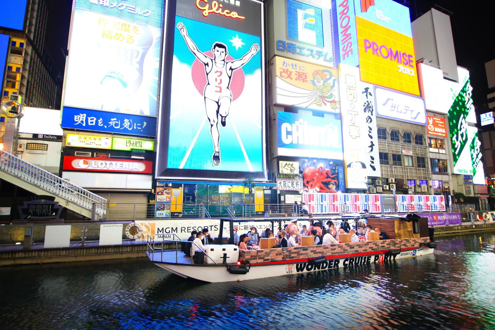 A covered sightseeing boat on the Dotonbori canal in Osaka, passing the illuminated signs